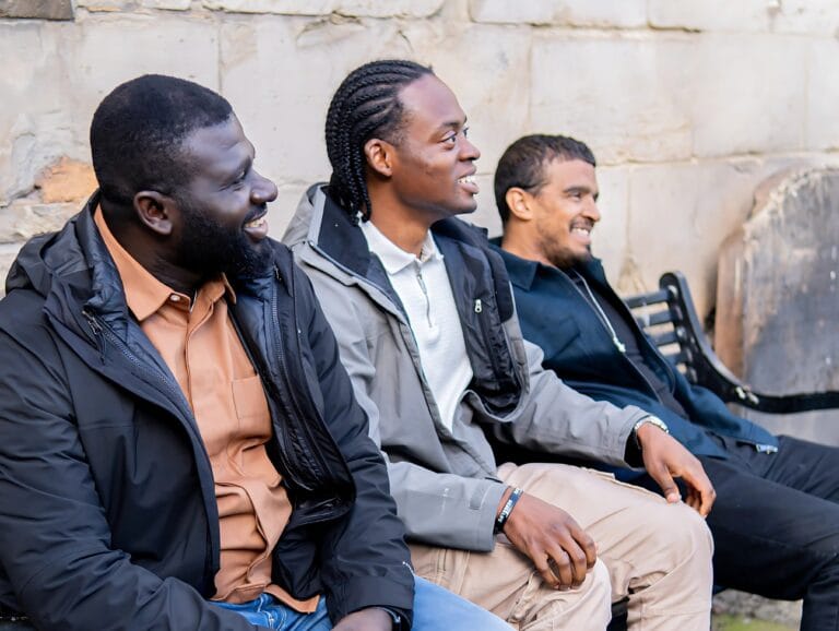 three-men-sitting-on-a-bench-smiling-and-enjoying-time-together-outdoors