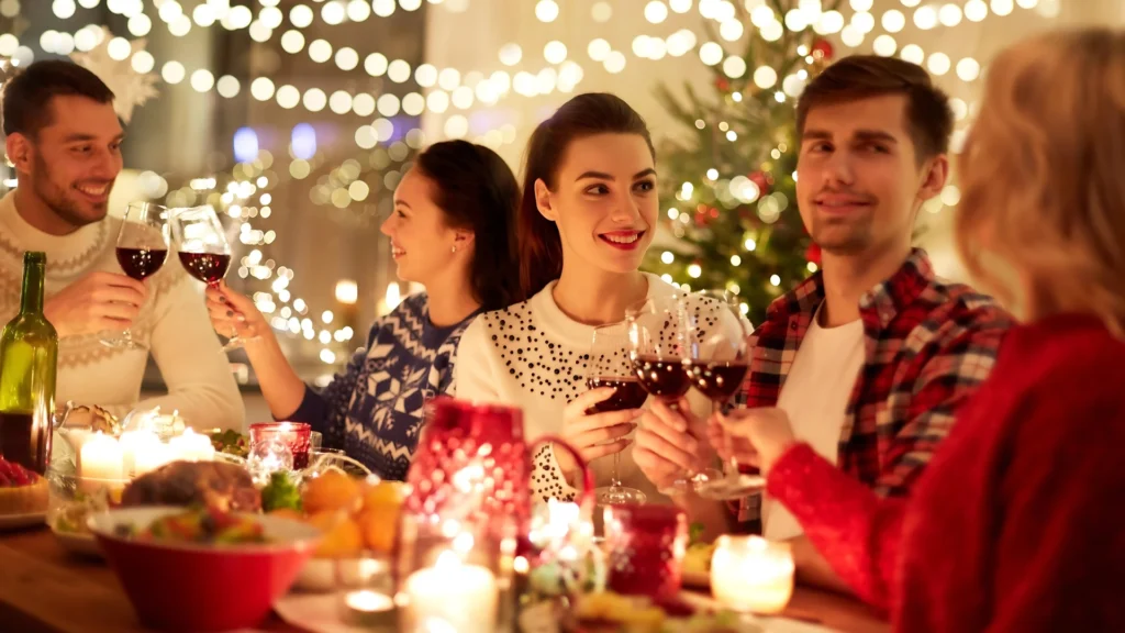 A-group-of-six-friends-at-a-festive-Christmas-party,-dressed-in-holiday-attire-with-props-such-as-Santa-hats,-fake-beards,-and-signs,-smiling-and-posing-for-the-camera-against-a-decorated-background-with-g