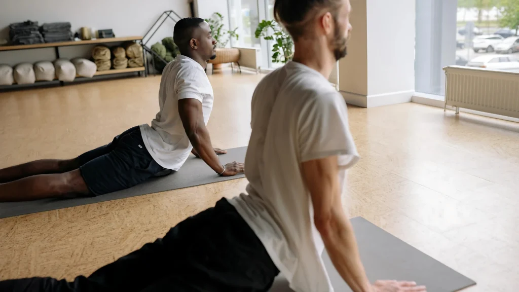 Two-men-doing-yoga-in-a-bright-studio,-practicing-a-cobra-stretch-on-yoga-mats-Healthy-Tips-for-the-Holidays-to-stay-active-and-relaxed