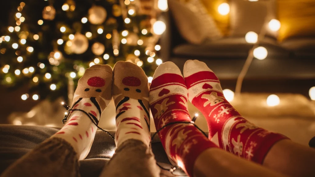 Two-people-wearing-festive-Christmas-socks-sitting-together-near-a-decorated-Christmas-tree-with-glowing-lights.