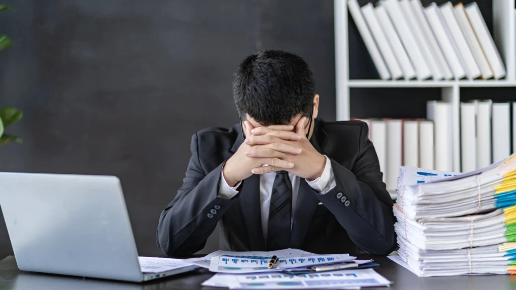 A-businessman-worried-about-money-sits-stressed-at-his-desk-surrounded-by-documents