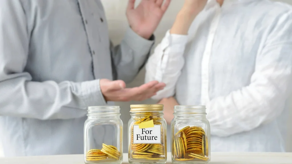 A-couple-worried-about-money-discussing-beside-jars-labeled-For-Future-filled-with-coins
