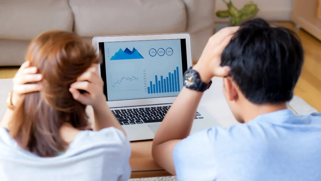 A-couple-worried-about-money-looks-at-a-laptop-displaying-declining-graphs-and-statistics