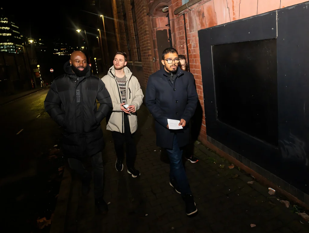 A-group-of-four-people-walking-at-night-holding-papers-with-buildings-and-streetlights-in-the-background-possibly-during-Season-2-Session-1-Mental-Health