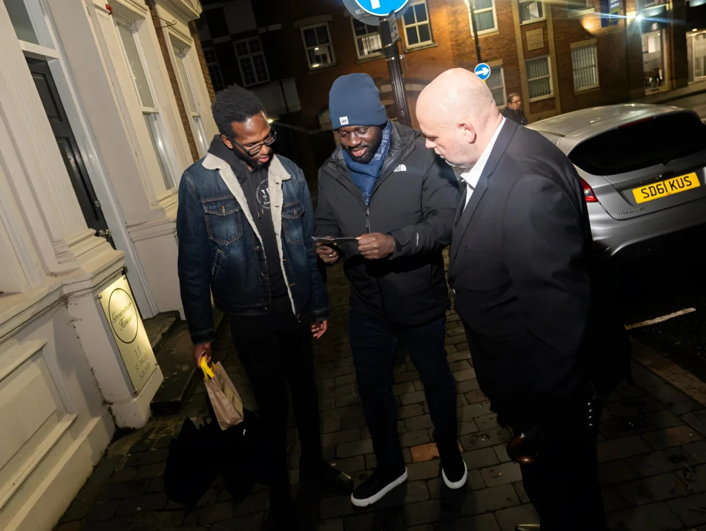 A-group-of-three-people-standing-outside-a-building-talking-to-each-other-with-a-car-in-the-background-possibly-during-Season-2-Session-1-Mental-Health