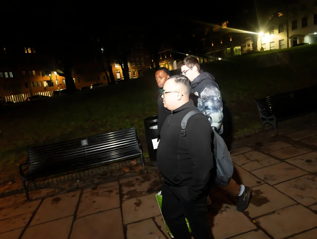 A-group-of-three-people-walking-at-night-near-a-bench-with-buildings-and-streetlights-in-the-background-possibly-during-Season-2-Session-1-Mental-Health