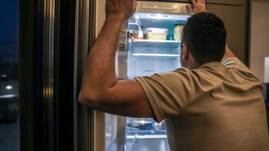 A-man-looking-into-a-refrigerator-at-night-depicts-the-Challenges-of-Mental-Health-and-Obesity