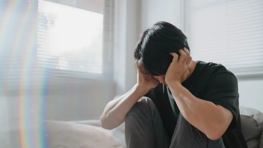 A-man-sitting-on-a-bed-holding-his-head-in-distress-with-soft-lighting-coming-through-a-window-symbolizing-anxiety-and-stress