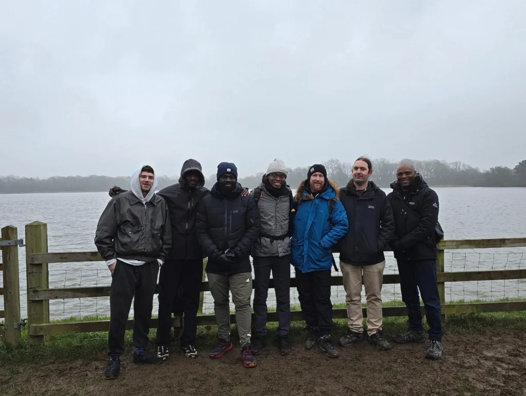 A-group-of-MPC-members-standing-together-by-a-lake-dressed-in-warm-clothing-enjoying-a-chilly-outdoor-moment