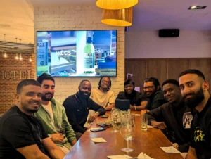 A-group-of-people-enjoying-a-meal-at-a-table-in-a-restaurant-with-a-TV-screen-in-the-background