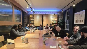 A-group-of-MPC-members-sit-around-a-long-wooden-table-having-a-discussion-in-a-cozy-modern-room-with-brick-walls-and-warm-lighting