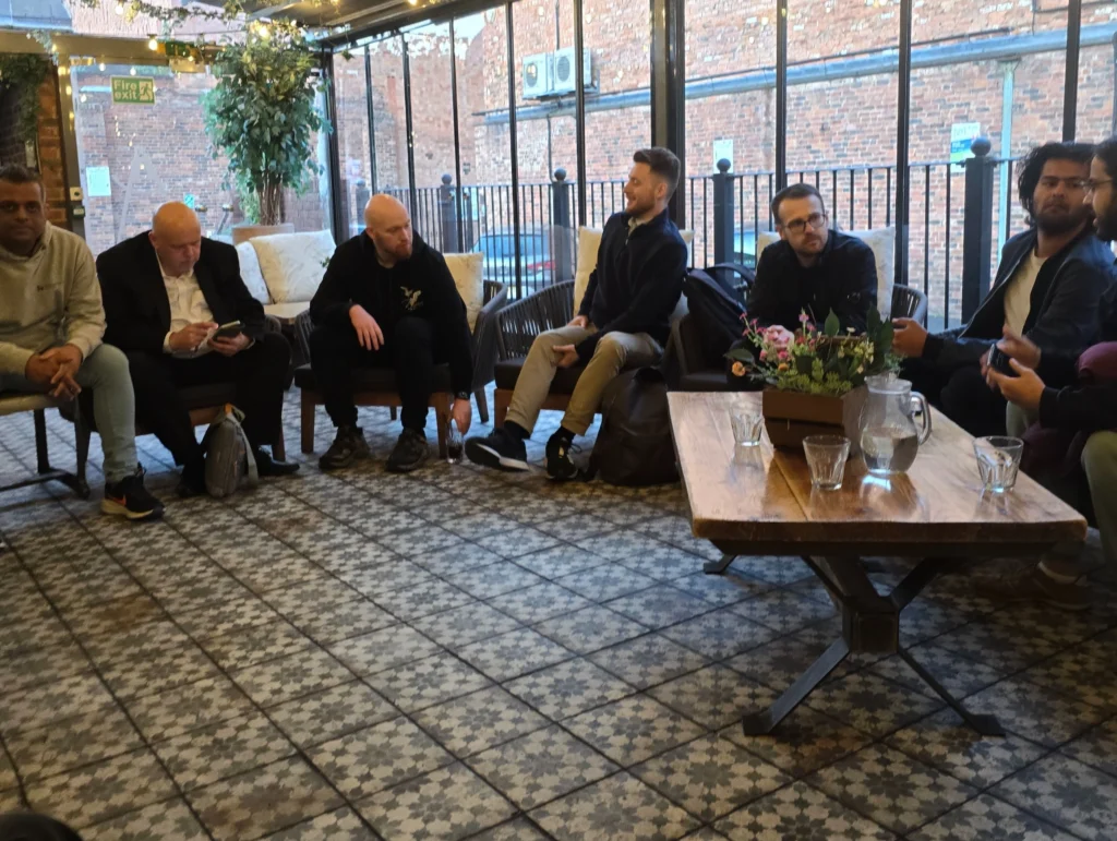 A-group-of-individuals-gathered-around-a-table,-having-a-conversation-in-a-relaxed-setting,-with-a-cozy-ambiance-and-decorative-lights