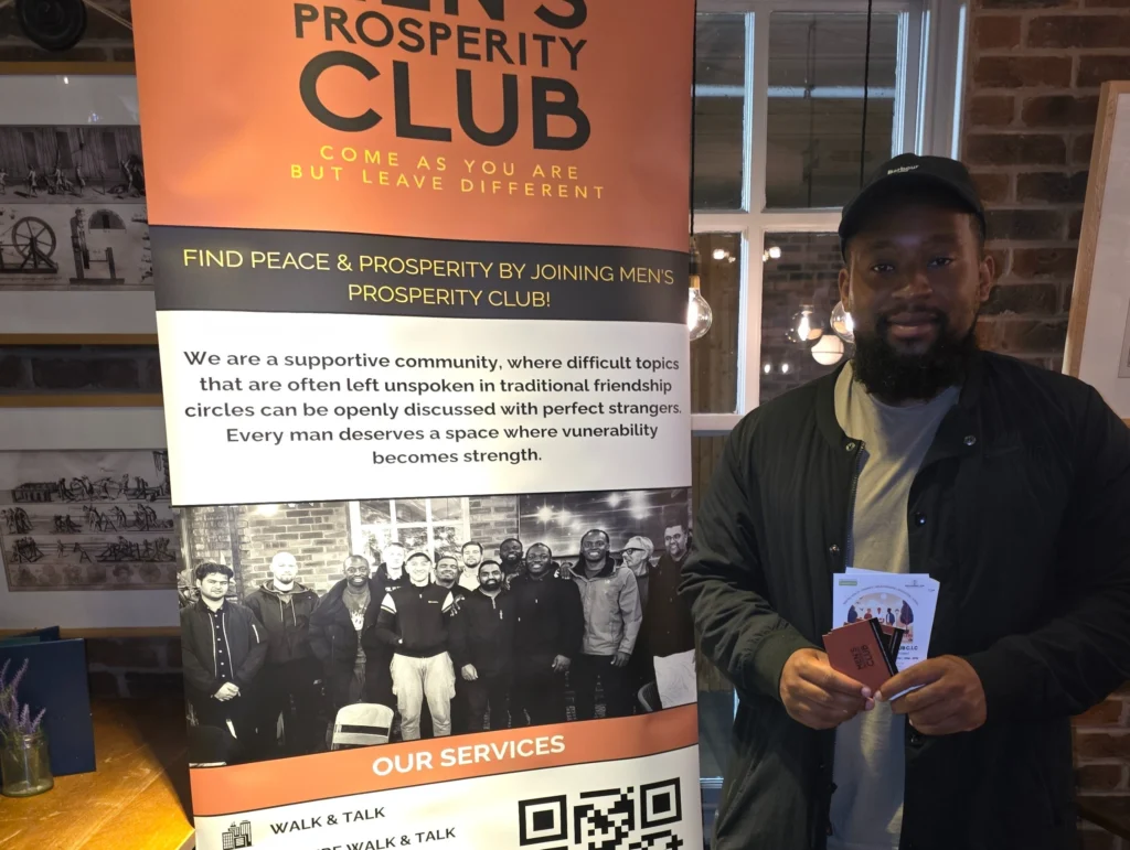 Man-standing-in-front-of-the-Men's-Prosperity-Club-banner,-holding-a-membership-card