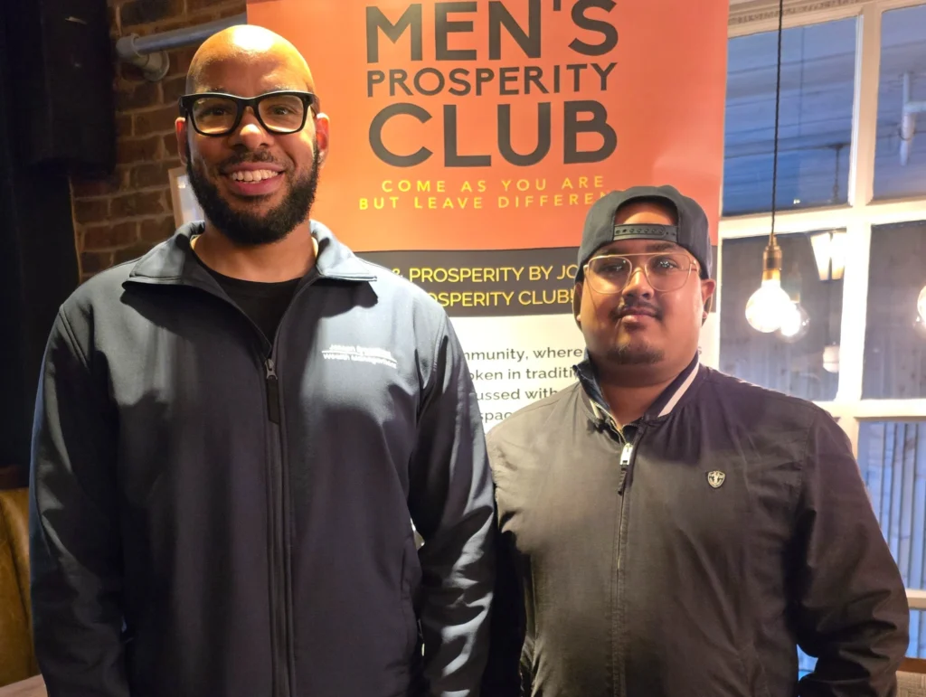 Two-men-standing-in-front-of-the-Men's-Prosperity-Club-banner-both-smiling