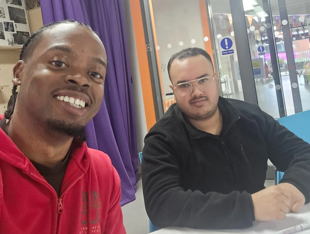 A-selfie-of-two-participants-at-the-PD-workshop-smiling-in-front-of-a-banner-for-Men's-Prosperity-Club