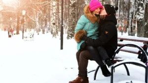 Couple-sharing-a-kiss-on-a-snowy-bench-celebrating-cuffing-season-together